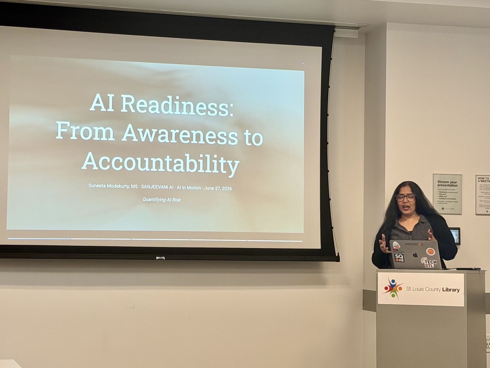 The projected title slide filling the library wall, with Suneeta at the lectern to the right.