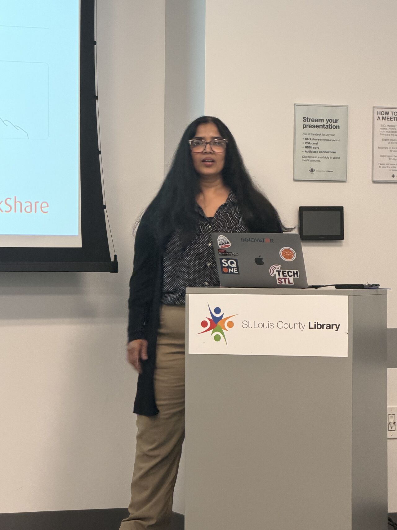 Suneeta at a St. Louis County Library lectern with her laptop open, mid sentence.