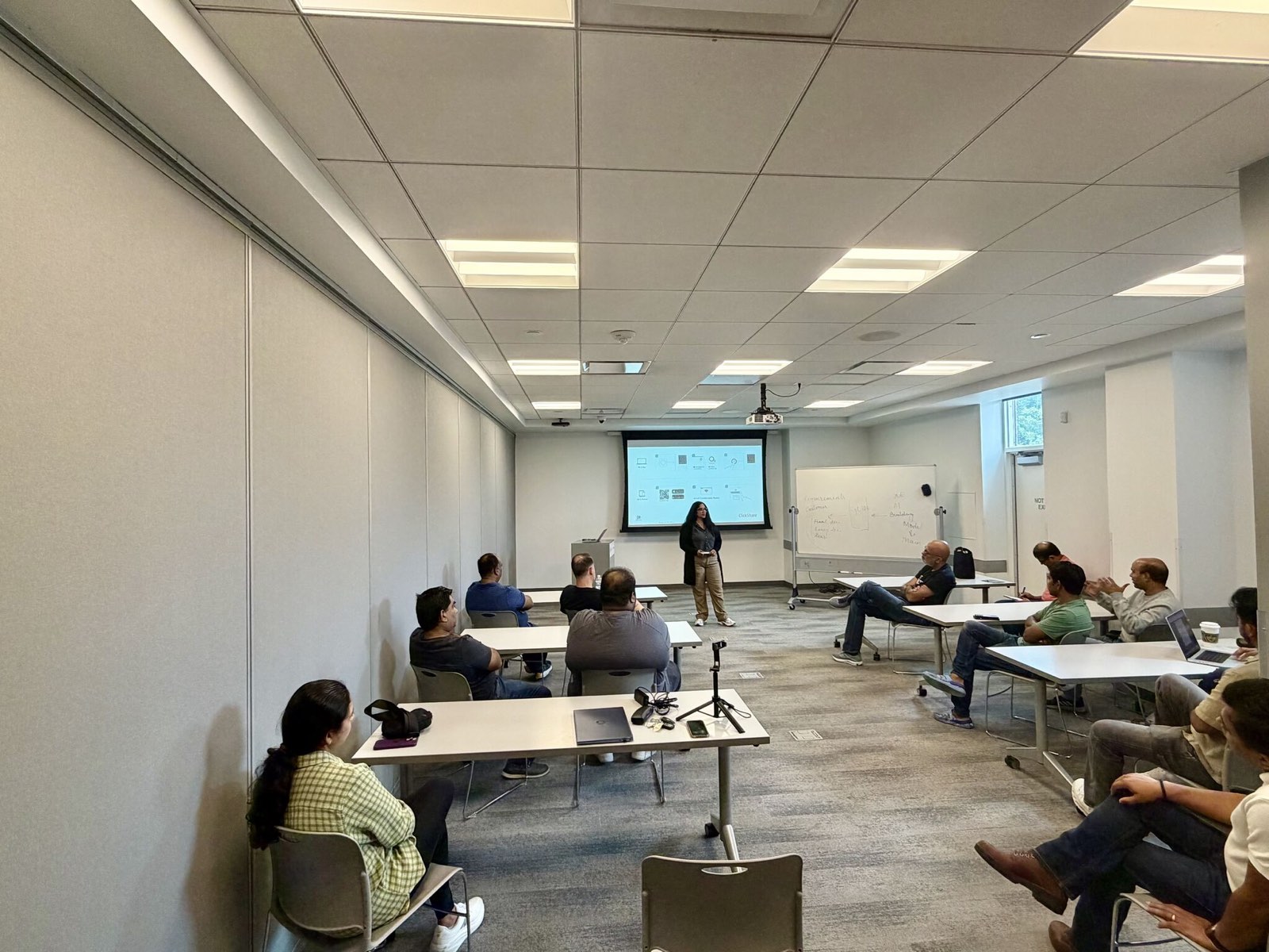 Wide view of the library meeting room, attendees seated at tables facing Suneeta at the front.