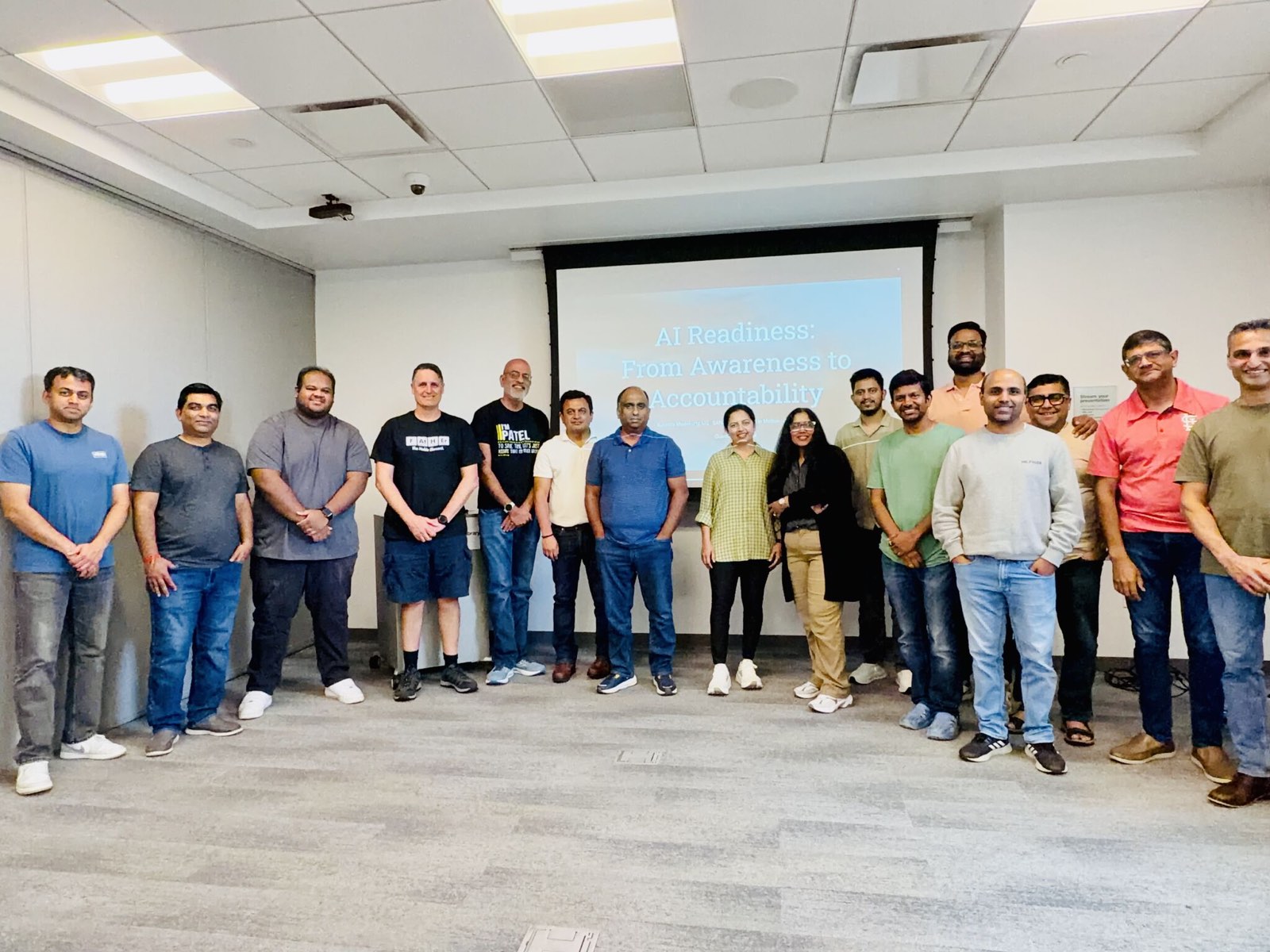 Group photo of about seventeen attendees standing together in front of the projection screen.