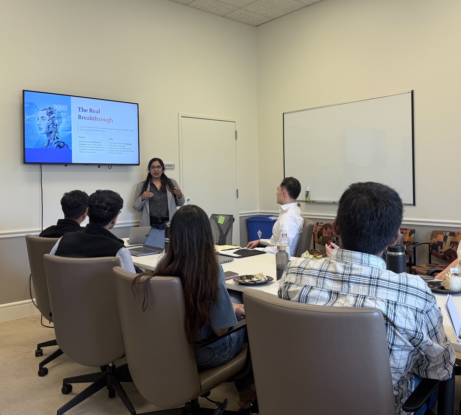 Suneeta presenting a slide to a group seated around a conference table.