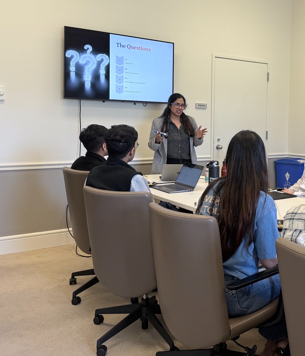 Suneeta gesturing toward a wall screen while attendees at the conference table look on.